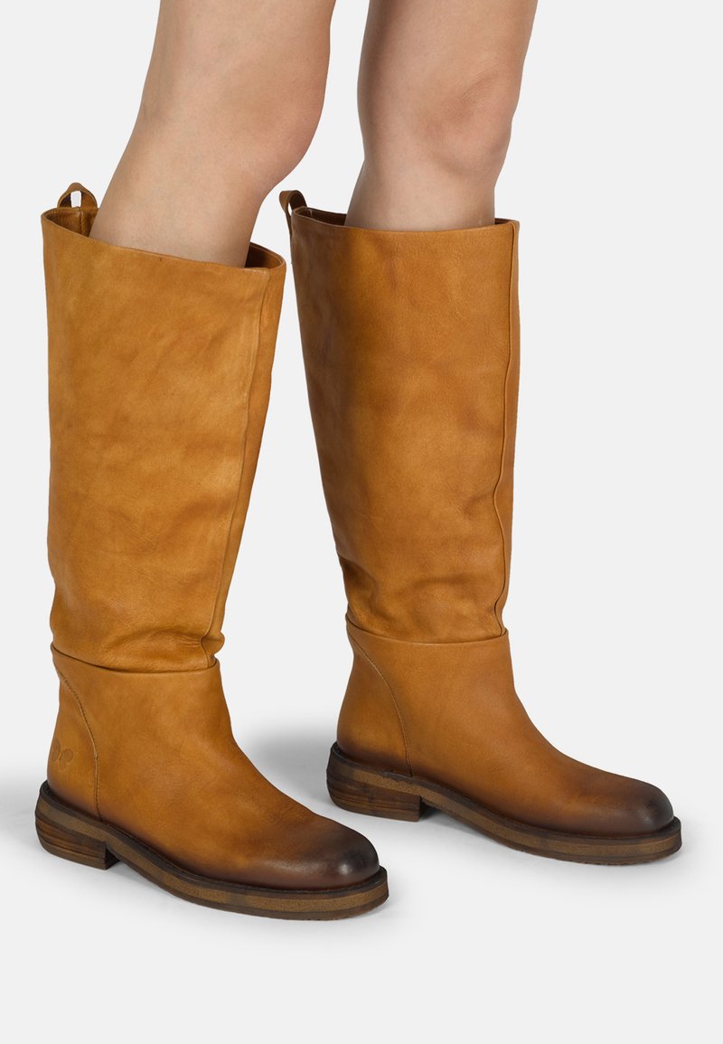 Botas de cuero marrón hasta la rodilla con un diseño ligeramente holgado, puntera redonda y tacón apilado. Acabado texturizado y tiradores en la parte superior.