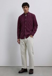 Bordeauxfarbene Hemd mit Knöpfen, weiße Hose und dunkelbraune Schuhe. Mittelschwerer Stoff, mit Kragen, schlichte Textur ohne Muster.