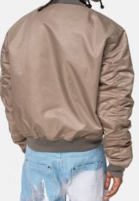 Brun nylon bomberjakke med ribbet ærmeafslutning og linning. Glat tekstur, let opsamlede ærmer og simpelt design.