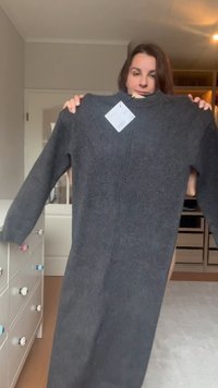 Tamno sivi oversize pulover haljina s dugim rukavima, rebrastim izrezom i pričvršćenom etiketom. Ima jednostavan dizajn i mekanu teksturu.