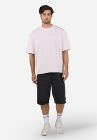 Light pink oversized t-shirt with a ribbed texture, paired with black knee-length shorts and white sneakers, featuring logo socks.