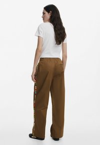Hnedé, široké nohavice s elastickým pásom, s farebnou pruhovanou stranou. Skombinované s jednoduchým bielym tričkom.