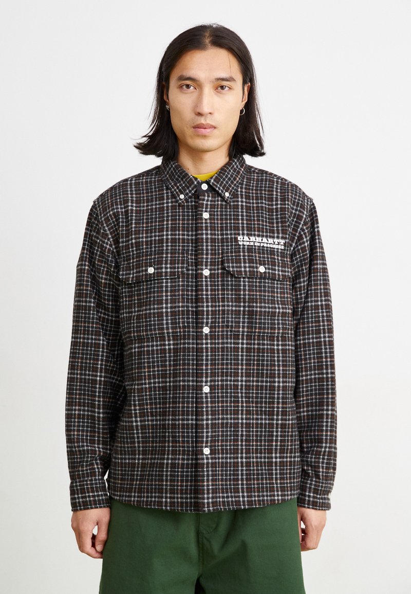 Chemise à carreaux noir et marron avec manches longues, col button-down, deux poches poitrine et détail de logo blanc sur le côté gauche.