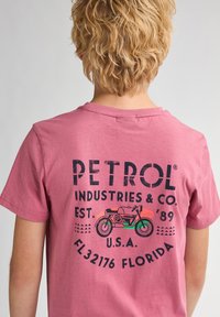 Lyserød bomulds t-shirt med grafik i sort af en motorcykel samt teksten: "PETROL INDUSTRIES & CO. EST. '89 U.S.A. FL32176 FLORIDA."
