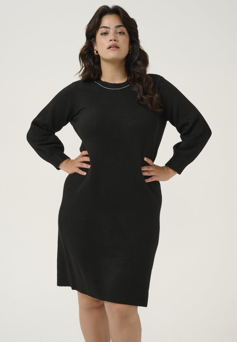 Black knitted dress with a round neckline, long sleeves, and side seam pockets. Smooth texture and knee-length hem. Simple design.