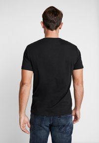 T-shirt en coton noir à manches courtes et décolleté rond. Le tissu est lisse et ajusté, présentant un design épuré et simple.