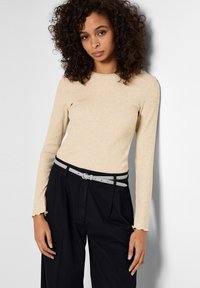 Top beige a coste con maniche lunghe e polsini svasati, abbinato a pantaloni neri a vita alta e una cintura grigia doppia.