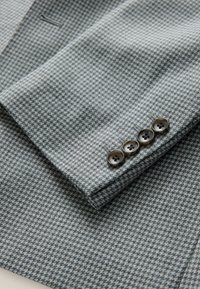 Gray houndstooth tailored blazer cuff with four brown buttons and a smooth texture, featuring subtle stitching details.