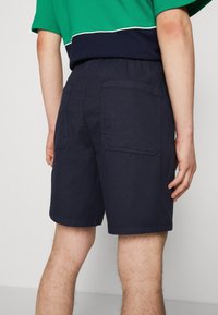 Pantalones cortos de algodón azul marino con una cinturilla elástica, que cuentan con dos bolsillos traseros y un corte recto. La textura parece suave y sin adornos.