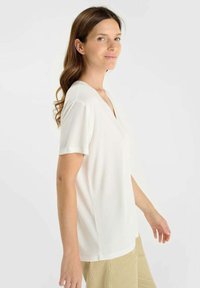 Witte korte mouwen V-hals T-shirt van zacht materiaal, gedragen met beige broek, met een relaxte pasvorm en lichte textuur.
