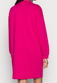 Robe sweat-shirt oversize fuchsia à manches longues, col rond et poignets côtelés. Texture douce, longueur genou, avec un design simple.