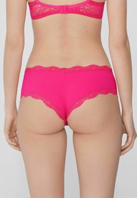 Jasnoróżowa bielizna z koronkowym wykończeniem w kwiaty. Posiada dopasowany, bezszwowy krój oraz falbany na brzegach. Materiał wydaje się być miękki i elastyczny.
