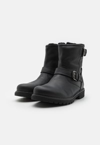 Schwarze Lederstiefeletten mit strukturiertem Finish, einem Schnallenakzent an der Seite und einer robusten Sohle, mit einem weichen Innenfutter, das oben sichtbar ist.