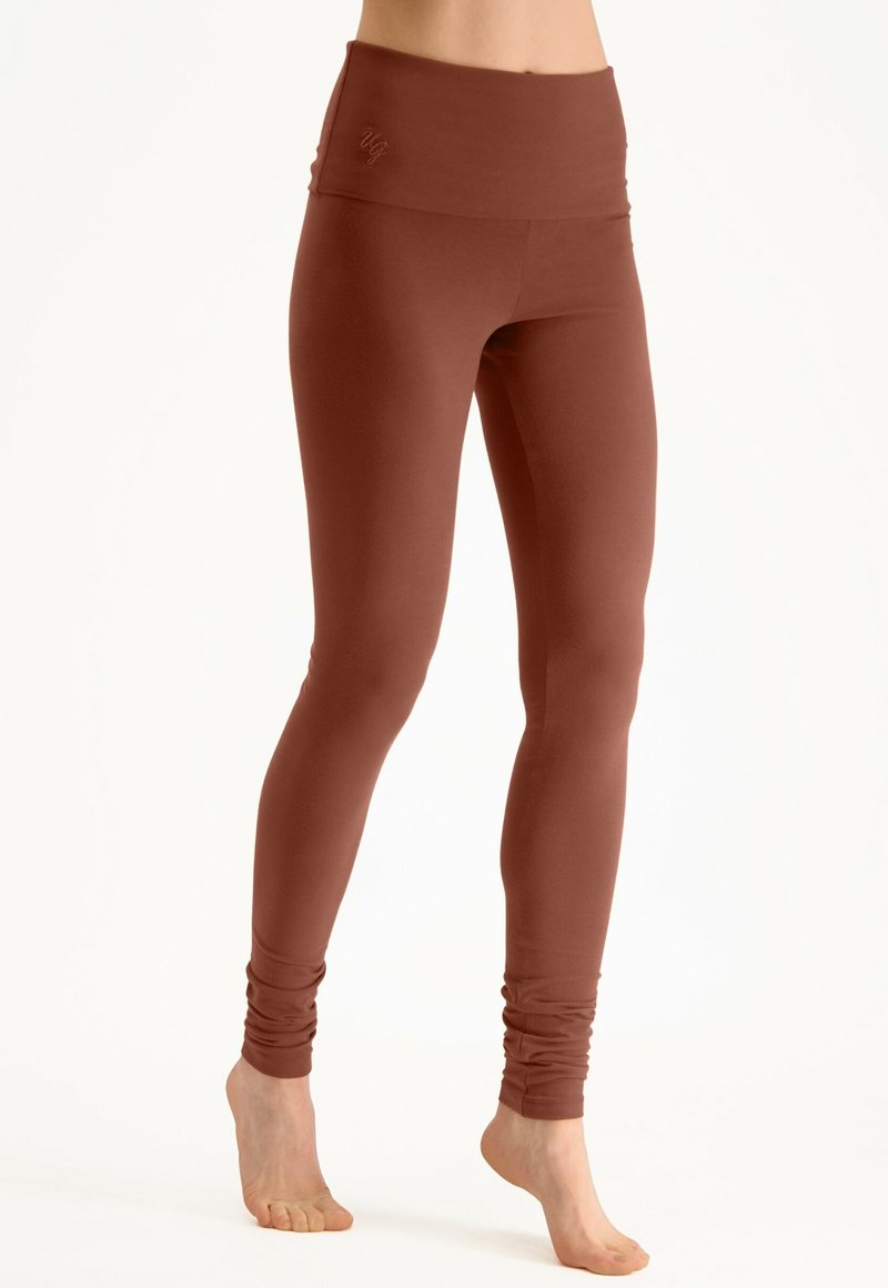 Leggings taille haute en couleur rouille foncé, fabriqués en matériau extensible avec une finition lisse, présentant un logo discret sur la ceinture.