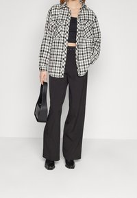 Sort og hvidternet skjorte med knapper, parret med en sort crop top og højtaljede sorte bukser. Model holder en lille sort håndtaske.