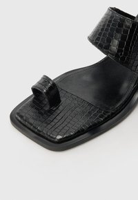 Sandale noire en simili cuir crocodile texturé, design ouvert, semelle plate et larges sangles pour maintenir le pied.
