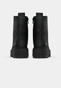 Black ankle boots with a textured leather exterior, sturdy rubber sole, and a prominent logo detail on the side. Features a zipper closure.