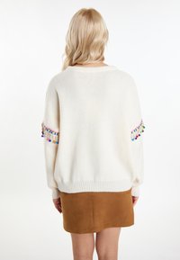 Witte gebreide trui met multicolor franjes op de mouwen, gecombineerd met een bruine suedine rok. Zachte textuur en een ontspannen pasvorm.
