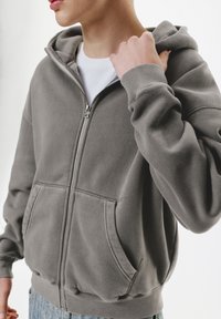 Gray zip-up hoodie made of soft fabric, featuring a large hood, front pockets, ribbed cuffs, and a relaxed fit.