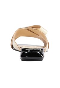 Flade sandaler med en sort patent hæl, gyldne metalstropper og en nude læder sål, designet med en åben bag for nemt at tage på.