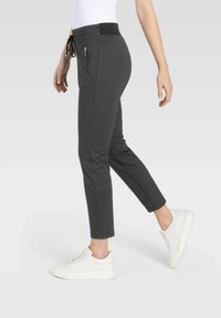 Graue Herringbone-Jogginghosen mit elastischem Bund, Kordelzug und seitlichen Reißverschlusstaschen, kombiniert mit weißen Sneakern.