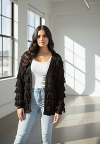 Czarny dziergany kardigan z frędzlami, z otwartym przodem, długie rękawy, w połączeniu z białą bluzką i jasnoniebieskimi, postarzanymi dżinsami.