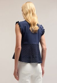 Navyblauw top met korte, gerafelde mouwen, voorzien van een getextureerde haakjesafwerking aan de achterkant en een licht uitlopende zoom, gecombineerd met witte jeans.
