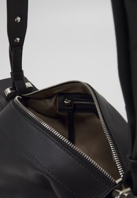 Borsa a mano in pelle nera con una tracolla spessa, accessori in argento e chiusura con zip. L'interno presenta una fodera beige e una tasca con zip.