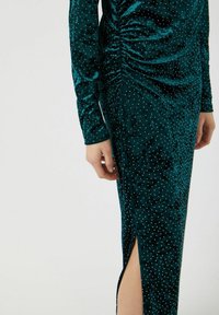 Tyrkysové sametové šaty s dlouhými rukávy, s řasením, zdobené stříbrnými hroty, se skluzem na boku, hladkou strukturou a přiléhavým střihem.