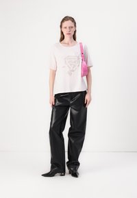 Lys rosa t-skjorte med korte ermer og grafisk trykk, kombinert med svarte bukser i imitert lær med vid ben og en glansfull rosa crossover-veske.