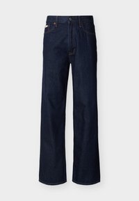 Σκούρο μπλε τζιν παντελόνι ίσιας γραμμής με πέντε τσέπες και κουμπί κλεισίματος, εμφανιζόμενο σε απλό φωτεινό φόντο.