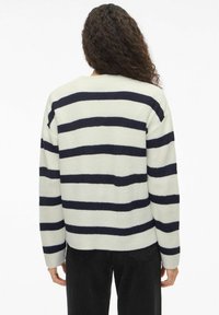 Pull rayé en crème pâle avec des rayures horizontales bleu marine. Tissu tricoté texturé, coupe décontractée, épaules tombantes et poignets côtelés.