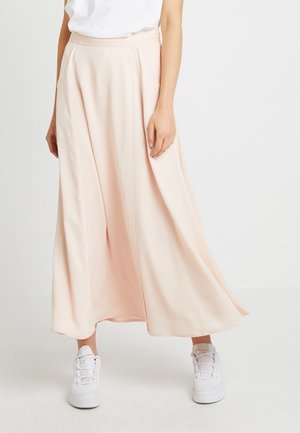 Flowing, ankle-length skirt in soft pink fabric with a smooth texture. Paired with white sneakers and a white t-shirt.