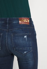 Jeans de mezclilla azul oscuro con una etiqueta dorada "ONLY" en la parte posterior de la cintura, que cuentan con dos bolsillos traseros y un sutil acabado desgastado.