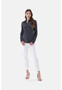 Navy button-up shirt with white polka dots, long sleeves, and a pointed collar; paired with white rolled-cuff trousers and nude heeled sandals.