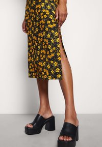 Svart blommig klänning med orange och gröna blommor, med en sidoklyvning. Bärs med kraftiga svarta klackskor.