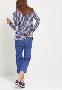 Gestreiftes Langarmhemd in Marineblau und Weiß, kombiniert mit einer mittelhohen blauen Jeans und lässigen marineblauen Sneakers. Fokus auf entspannter Passform und Textur.