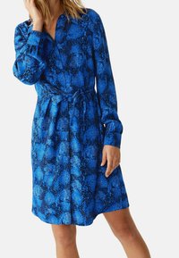 Abito camicia con stampa serpente blu, maniche lunghe, chiusura con bottoni e cintura da annodare in vita; realizzato in tessuto liscio con un motivo testurizzato.