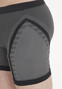 Grå sportboxerunderkläder har ett strukturerat tyg med geometrisk design, svart elastisk midjeband och kontrasterande mönstrade sidopaneler.