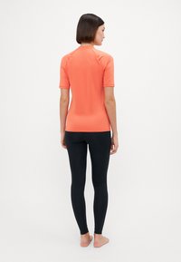 Korte ermer koralltop med rund halslinning, parret med svarte leggings. Glatt, elastisk stoff; tettsittende design; bakview.