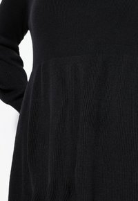 Abito nero a maglia con corpetto aderente e gonna svasata e testurizzata. Presenta maniche lunghe e un motivo a coste uniforme.