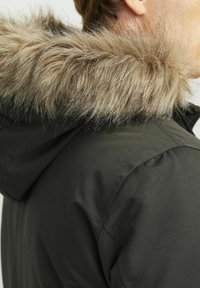 Donkergroene parka met een afneembare nep-bont capuchon, met een zachte, pluizige textuur en een strakke stofafwerking.