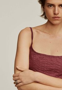 Vestido burdeos sin mangas con escote cuadrado, tejido texturizado y detalles de costura vertical. La modelo tiene los brazos cruzados, mostrando un anillo.