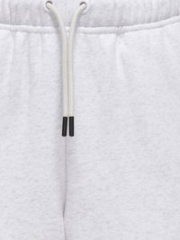 Gros plan sur la taille d'un pantalon de survêtement gris clair avec un cordon blanc et des embouts en plastique noir, centrée sur un tissu doux.