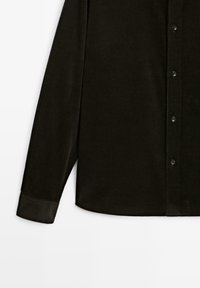 Sort corduroy skjorte med knap-til-forside, lange ærmer og en struktureret overflade med ribbede mønstre.