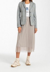 Sjekket blazer med blå, hvid og sort mønster, gennemsigtig plisseret grå midi-nederdel og beige sneakers med strukturering på sålen og cremede sokker.