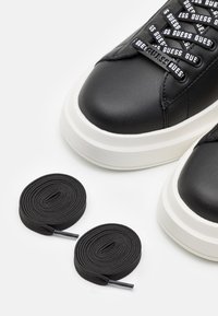 Schwarze Leder-Sneaker mit einer weißen, dicke Sohle, ausgestattet mit gebrandeten Schnürsenkeln. Enthält zwei Rollen schwarzer Schnürsenkel.