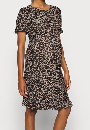 Gravid kvinde iført en knælange kjole med leopardprint, korte ærmer og flæsekant forneden og ved ærmekanterne, stående mod en ensfarvet baggrund.