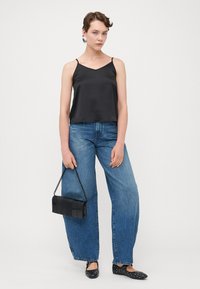 Svart sateng cami med tynne stropper, sammen med vide blå denimjeans. Modellen holder en liten svart veske med kjedehåndtak.