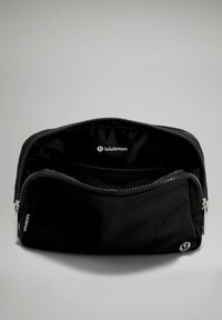 Bolsita de tela negra con cierre de cremallera, que presenta una textura suave y un bolsillo de malla en el interior. El logo de Lululemon es visible en el interior y en el lateral.